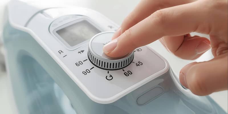Hand adjusting the thermostat of a modern electric iron with steam rising.